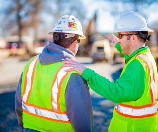 Two construction workers talking on a construction site.