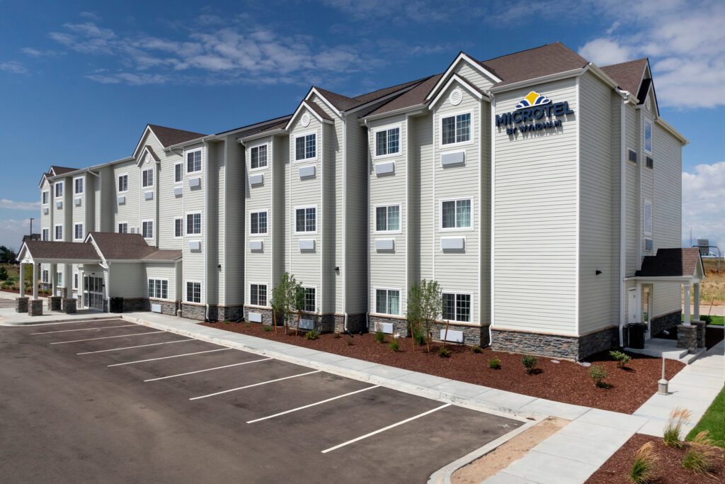 A modern three-story Microtel Inn & Suites hotel with white siding, several windows, a pitched roof, and an empty parking lot in front under a partly cloudy sky.