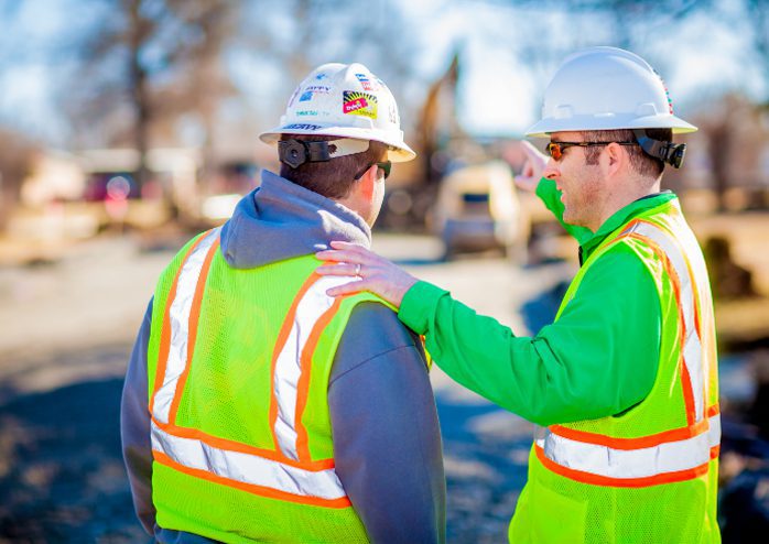 Two construction workers wearing PPE outside.