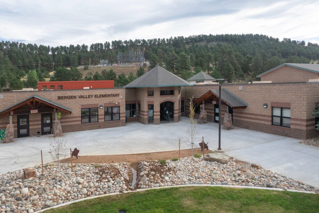 A wide view of Bergen Valley Elementary School, showing a modern brick building with a central entrance, surrounded by rocky landscaping and trees in the background.