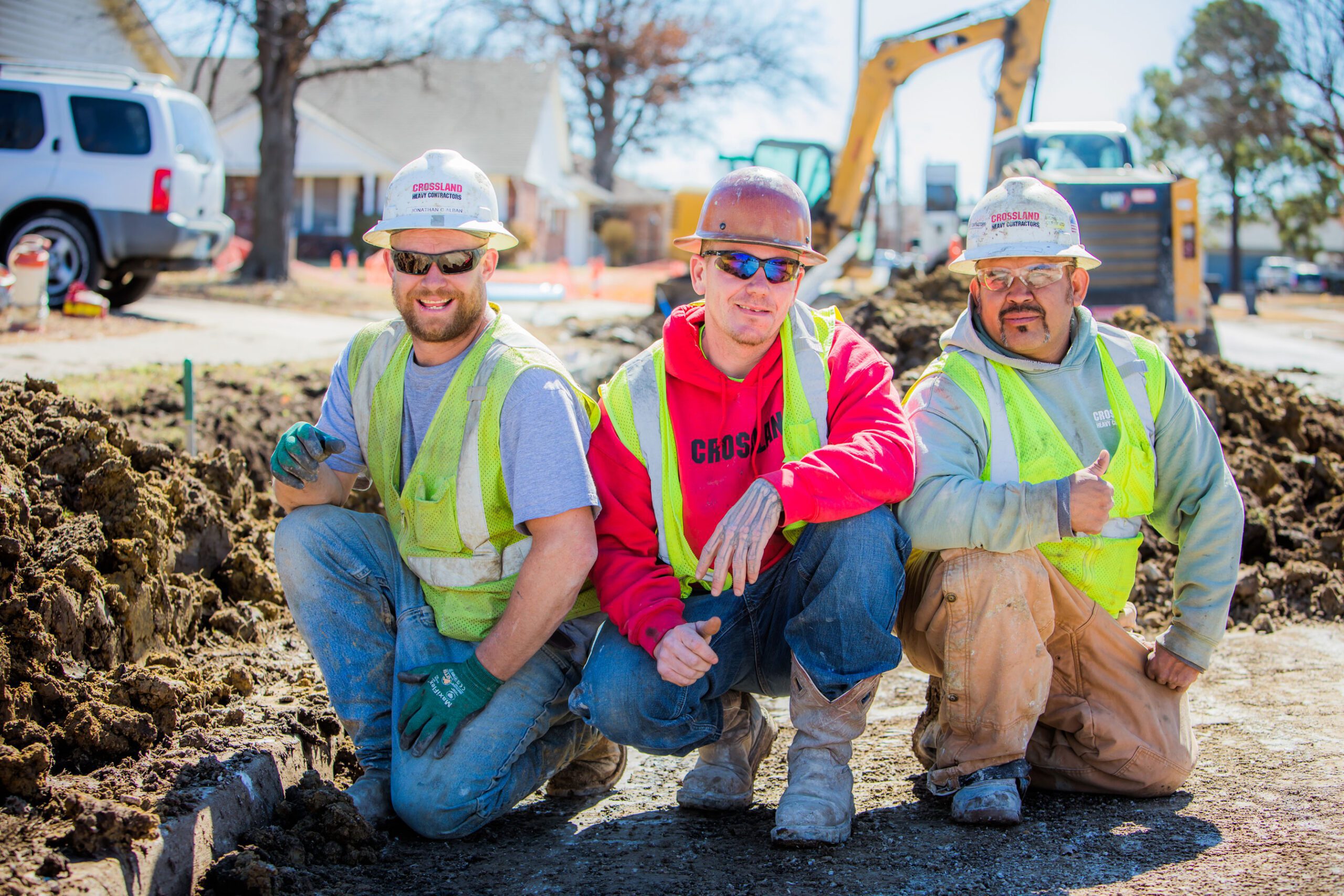 Three man pipe crew wearing PPE and smiling beside the job site.