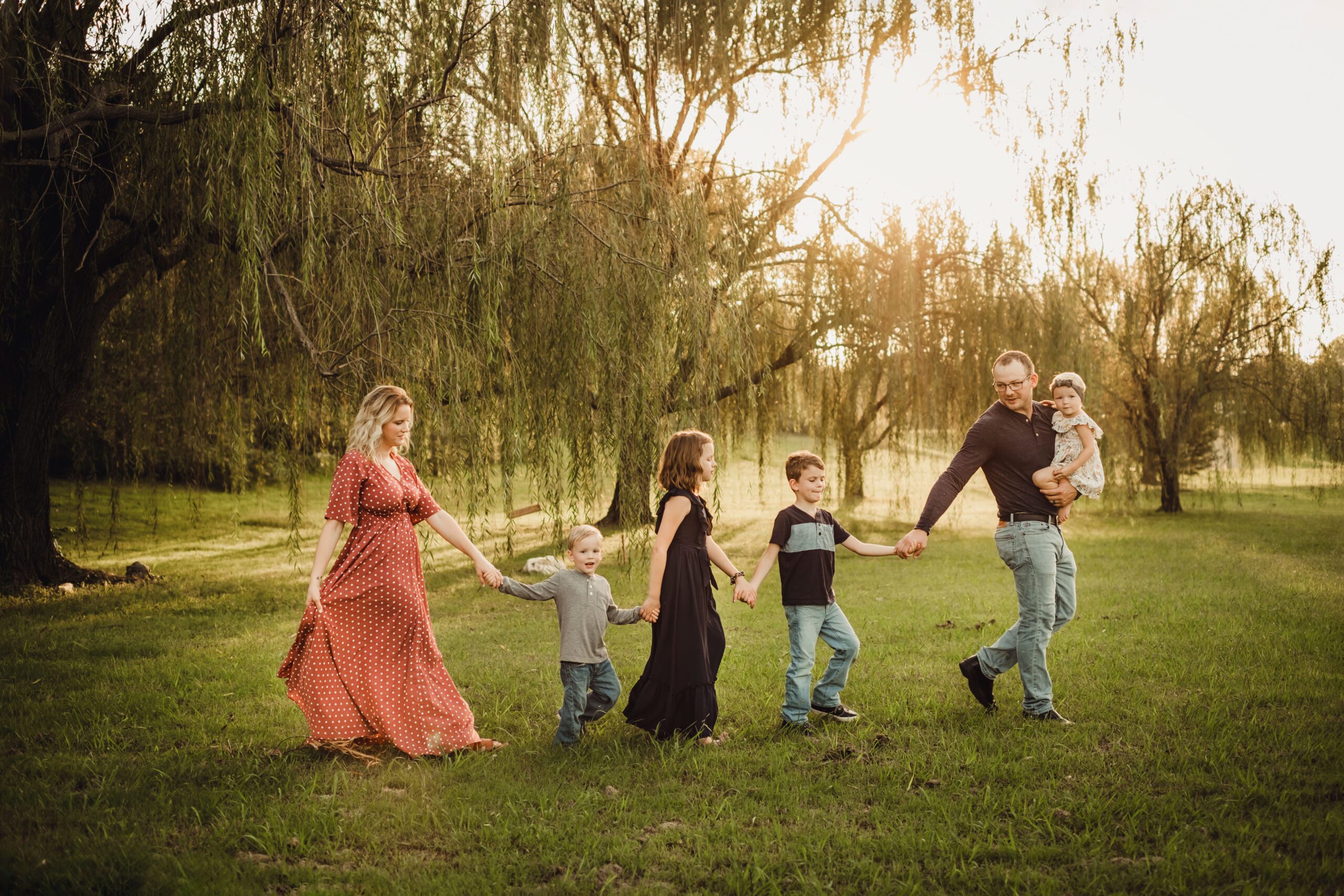 A family holding hands in a field at sunset.