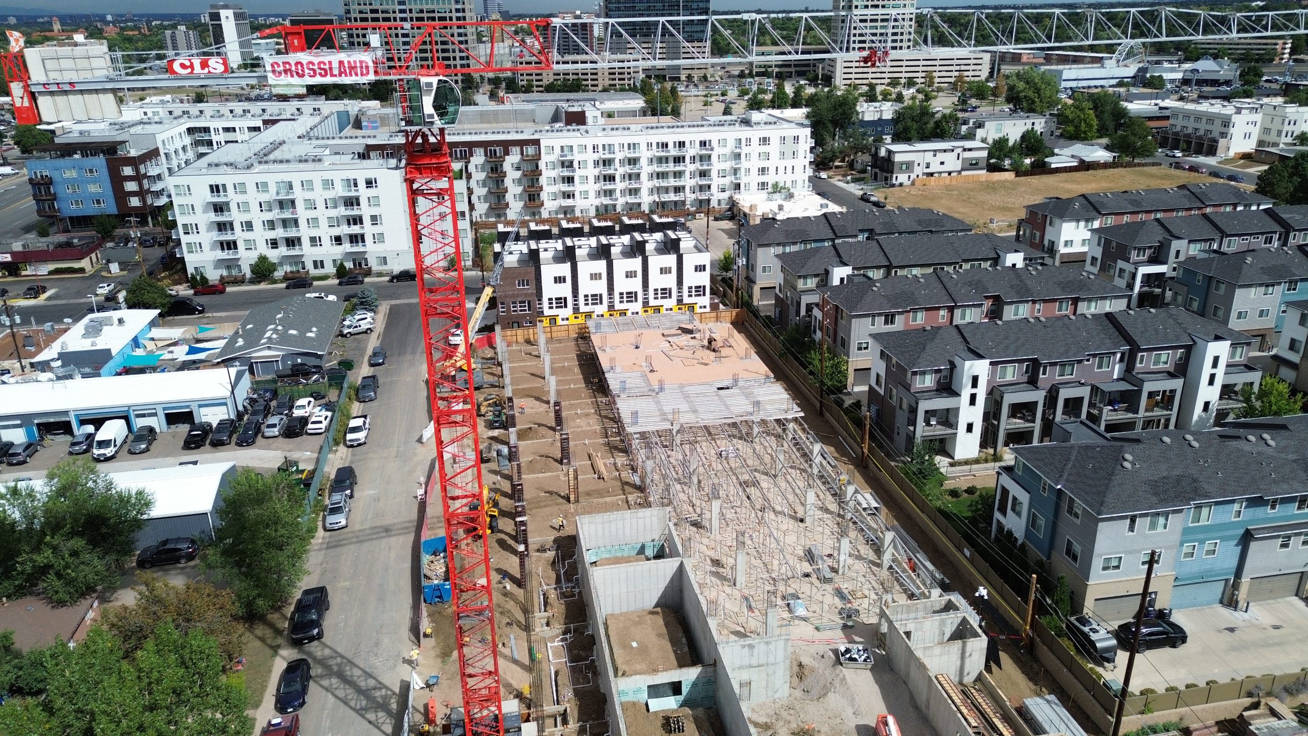 Aerial view of a construction site with a red crane labeled “GROSSLAND” beside partially built structures, surrounded by modern apartment buildings and city streets.