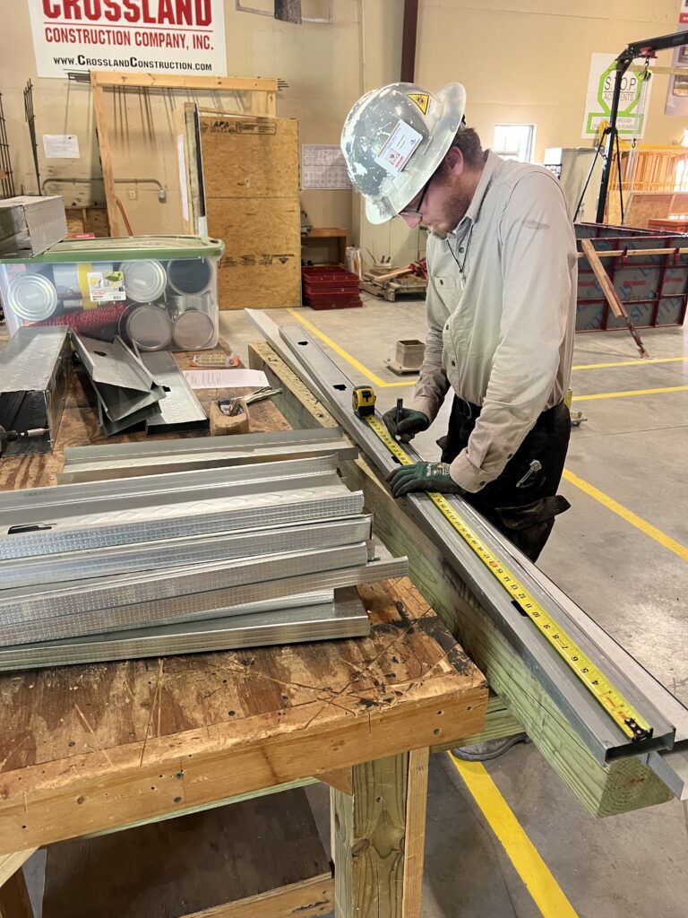 A man in a hard hat is measuring a piece of metal.