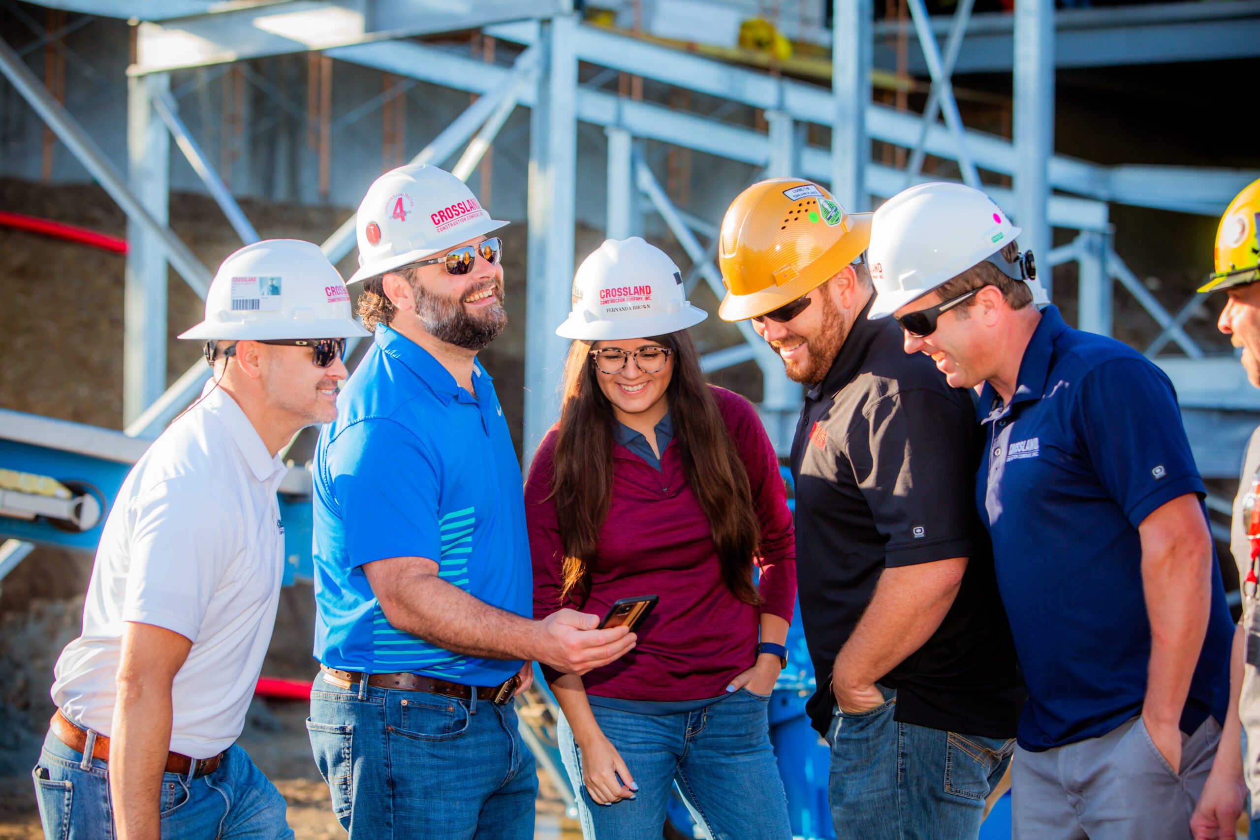 A group of people in hard hats looking at a cell phone.