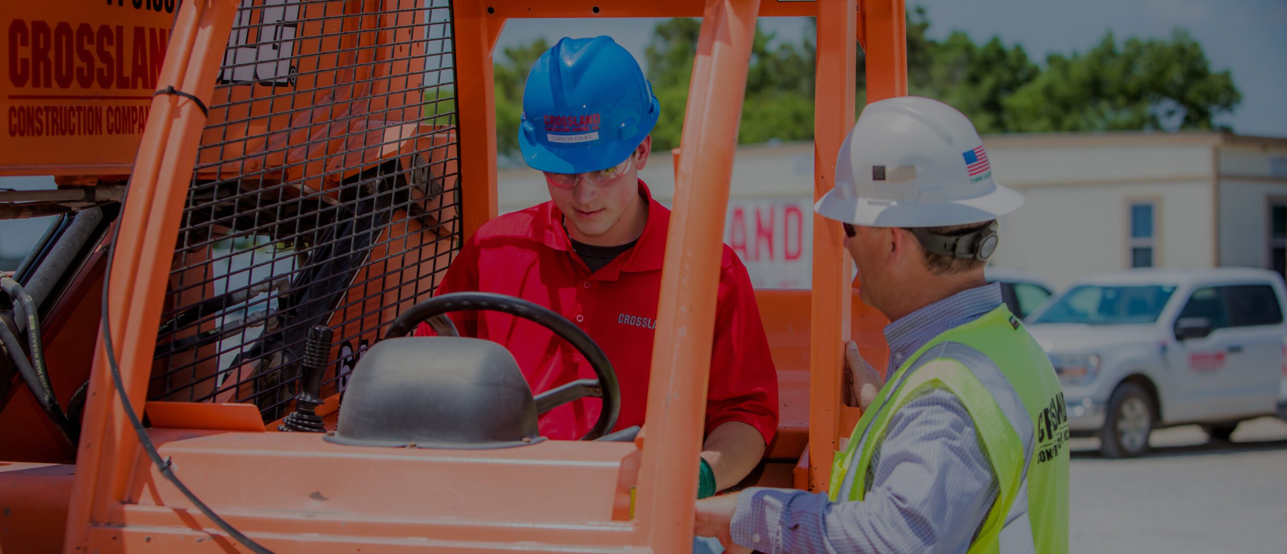 Two men in hard hats working on a forklift.